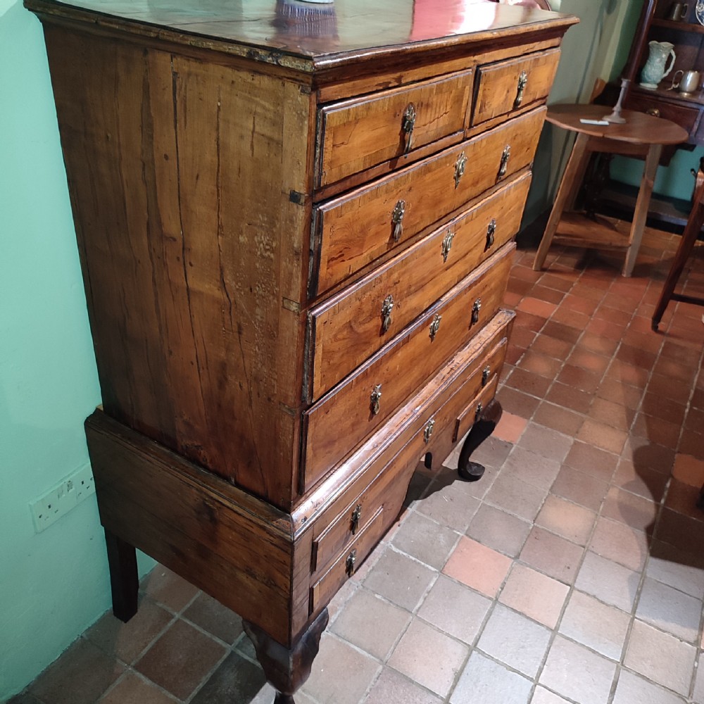 An antique Queen Anne yew wood chest on stand with crossbanded drawers, brass drop handles, and an arched apron raised on cabriole legs. View II