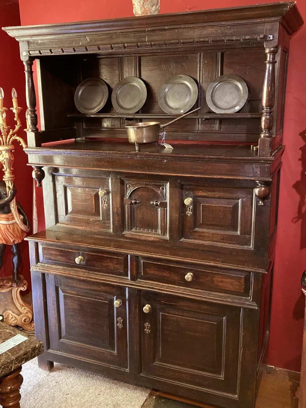 An early eighteenth-century dark oak three-tier Welsh tridarn featuring an open upper canopy, panelled cupboard doors, drawers, and turned balusters.