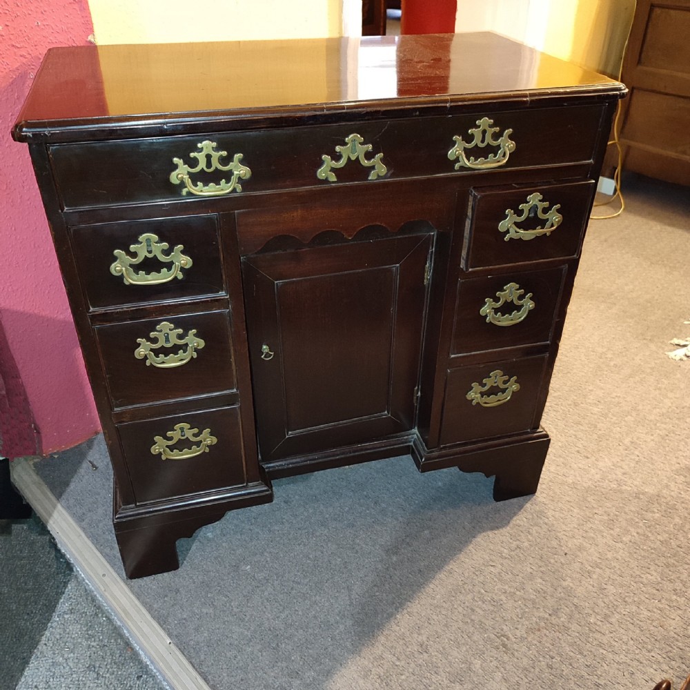 An 18th-century dark mahogany kneehole desk featuring brass batwing handles, a long top drawer, side drawers, a central recessed cupboard, and bracket feet.