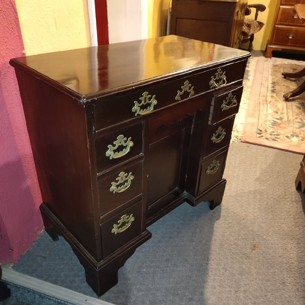An 18th-century dark mahogany kneehole desk featuring brass batwing handles, a long top drawer, side drawers, a central recessed cupboard, and bracket feet. View II