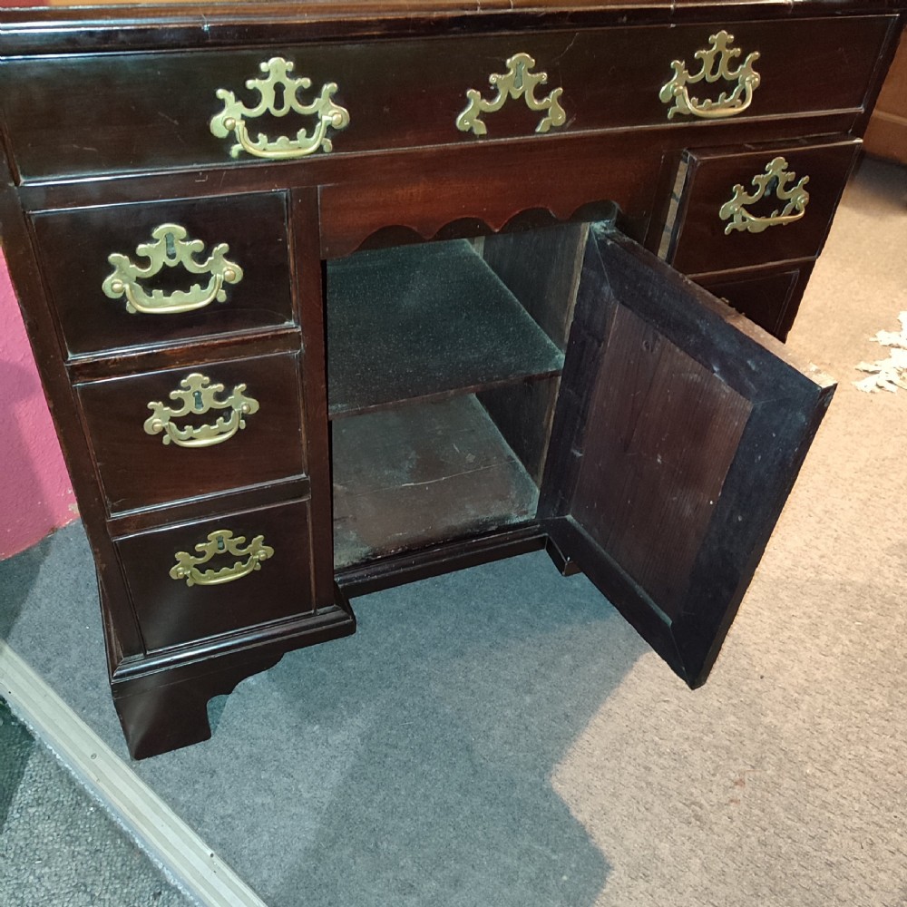 An 18th-century dark mahogany kneehole desk featuring brass batwing handles, a long top drawer, side drawers, a central recessed cupboard, and bracket feet. View IV
