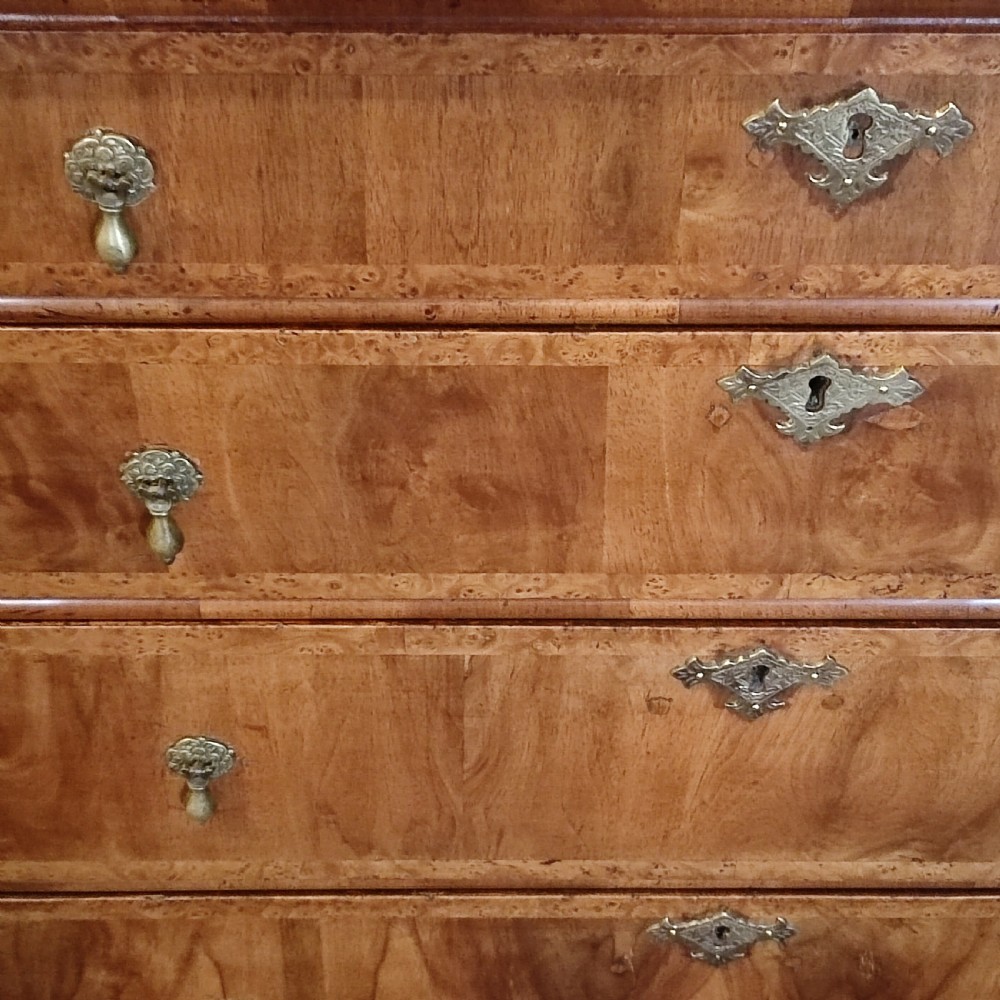 A George I period warm brown walnut chest of drawers featuring figured grain, crossbanded drawer fronts, brass drop handles, and bracket feet. View VI
