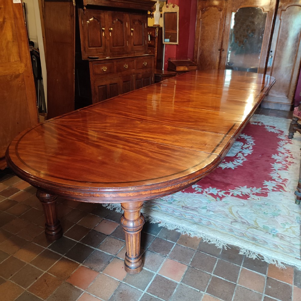 A large Victorian extending mahogany dining table featuring a polished surface with crossbanded inlay and turned fluted legs.