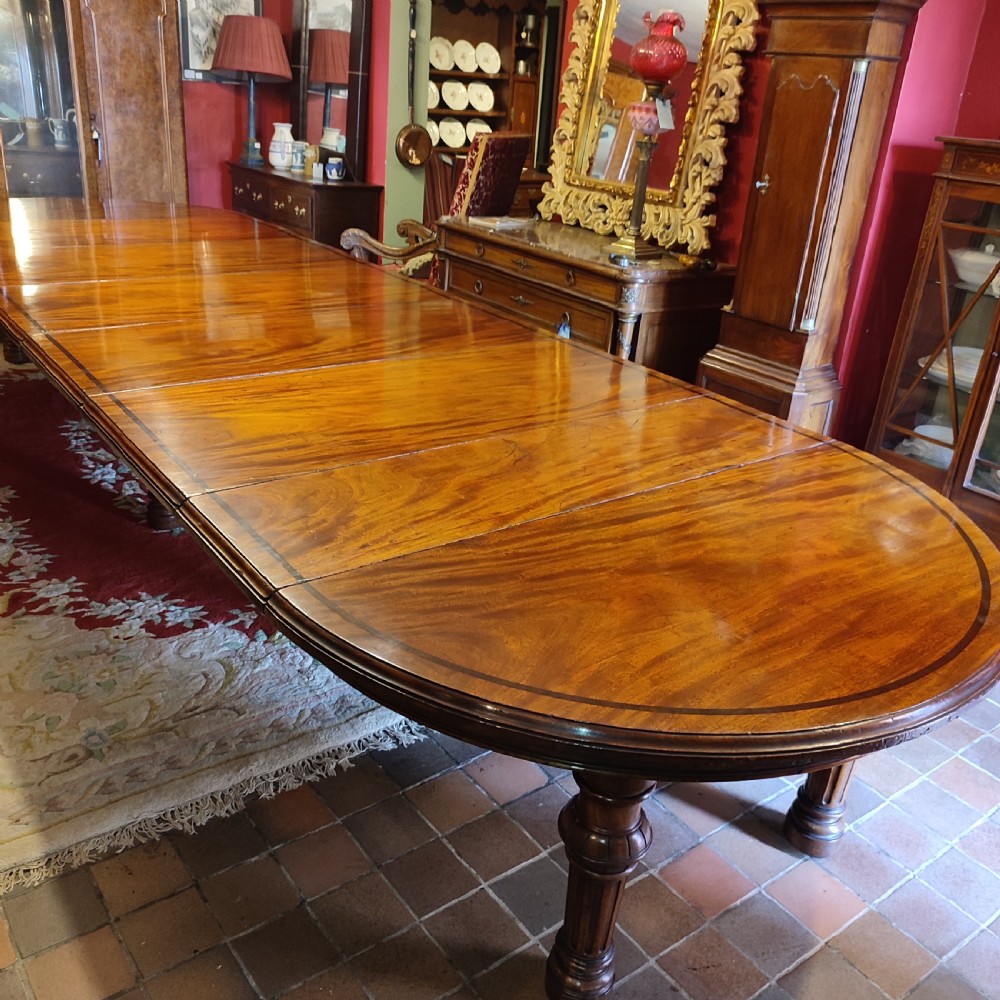 A large Victorian extending mahogany dining table featuring a polished surface with crossbanded inlay and turned fluted legs. View V