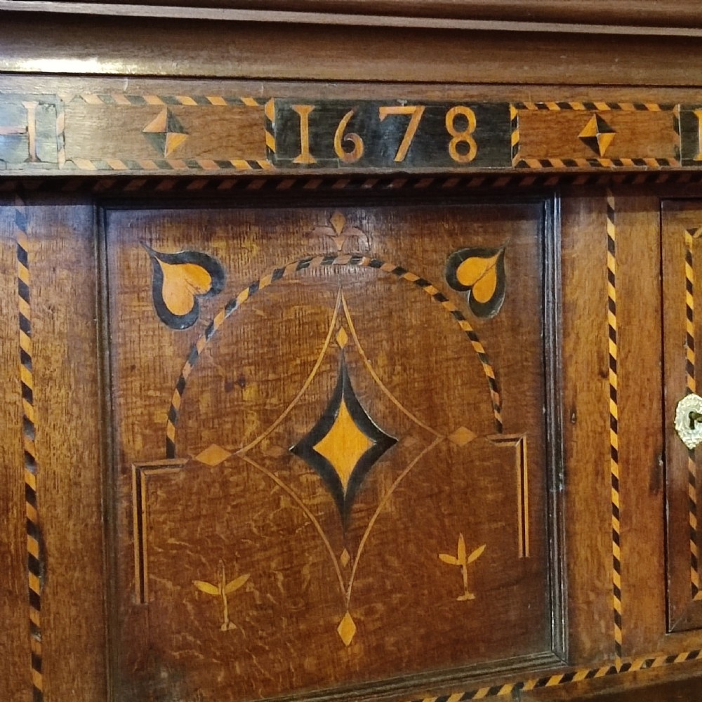 A seventeenth-century inlaid oak court cupboard featuring geometric marquetry, turned supports, and the carved date 1678 on the upper frieze. View III