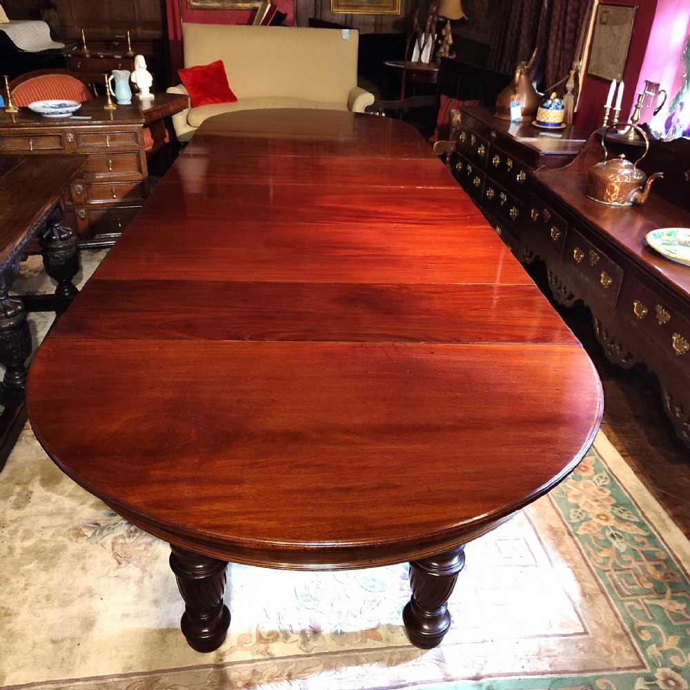 A large 19th-century mahogany extending dining table featuring a polished surface, rounded ends, and thick turned legs on casters.