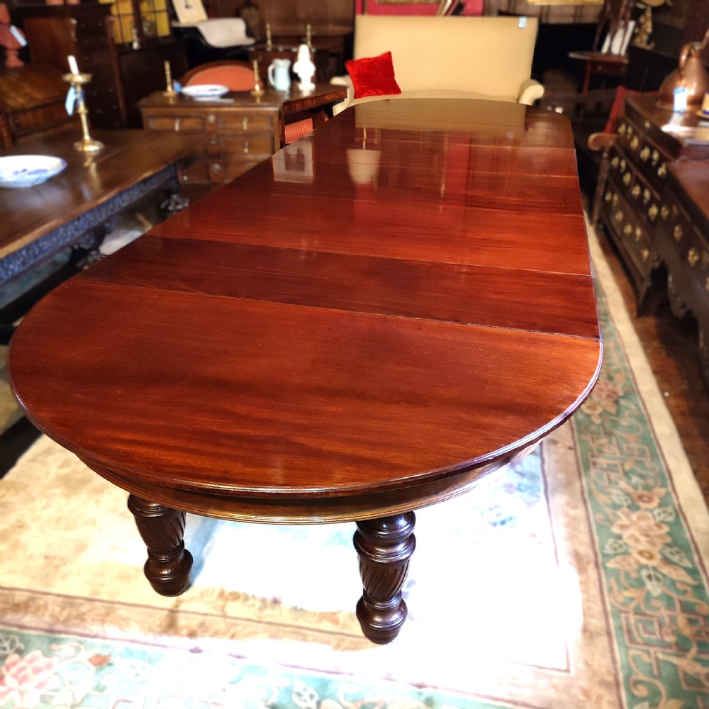 A large 19th-century mahogany extending dining table featuring a polished surface, rounded ends, and thick turned legs on casters. View II