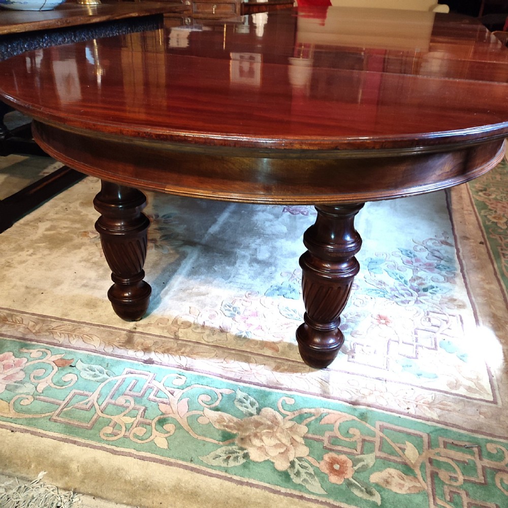A large 19th-century mahogany extending dining table featuring a polished surface, rounded ends, and thick turned legs on casters. View III