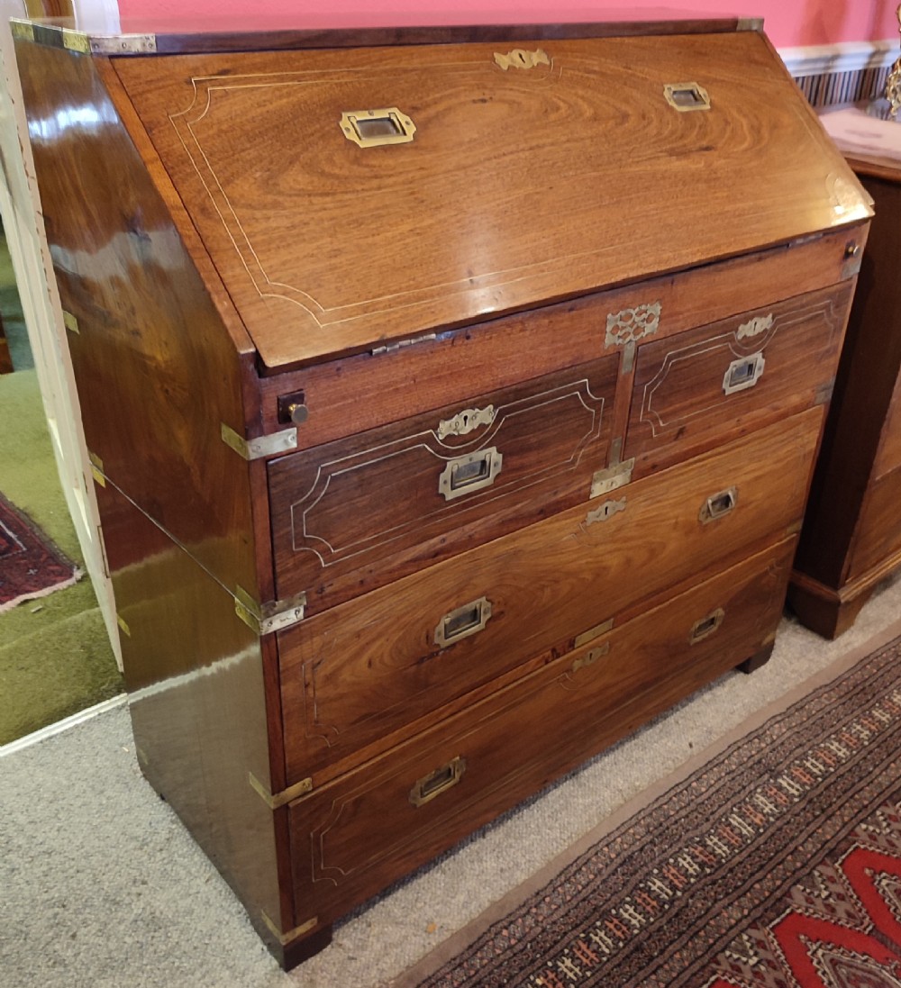 A nineteenth-century padouk wood campaign bureau featuring brass inlay, flush brass drawer handles, protective brass corner brackets, and a slanted fall-front writing flap.