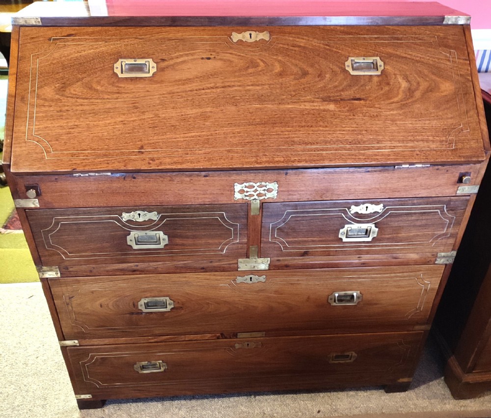A nineteenth-century padouk wood campaign bureau featuring brass inlay, flush brass drawer handles, protective brass corner brackets, and a slanted fall-front writing flap. View II