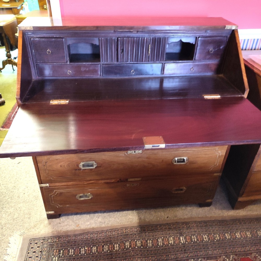 A nineteenth-century padouk wood campaign bureau featuring brass inlay, flush brass drawer handles, protective brass corner brackets, and a slanted fall-front writing flap. View IV