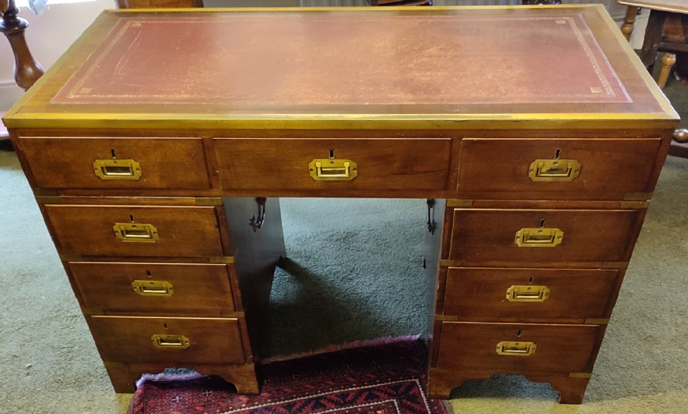 An Edwardian mahogany campaign pedestal desk featuring flush-fitting brass handles, protective brass corner mounts, and a red leather inset writing surface.
