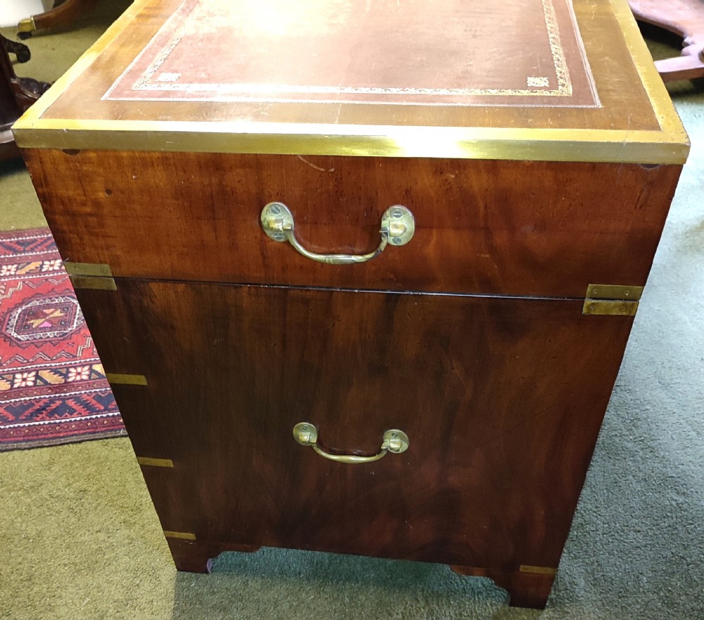 An Edwardian mahogany campaign pedestal desk featuring flush-fitting brass handles, protective brass corner mounts, and a red leather inset writing surface. View II