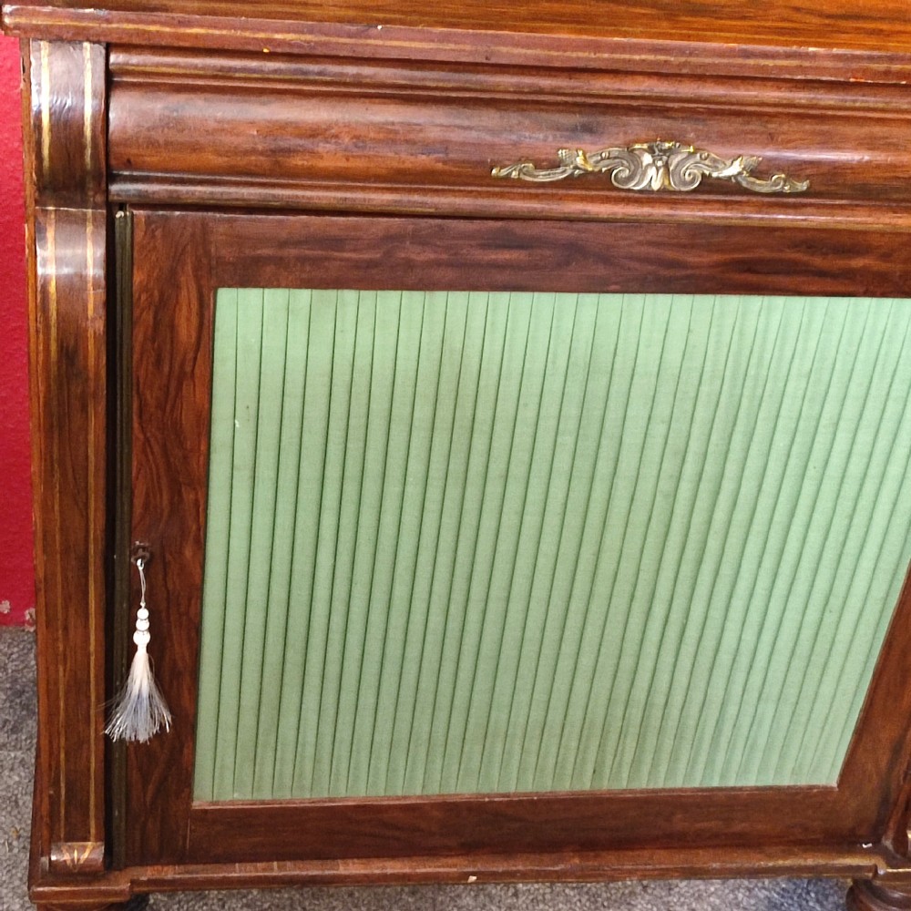 A Regency simulated rosewood chiffonier featuring a raised gallery shelf on S-scroll supports, gold line detailing, and a lower door with a pleated green fabric panel. View III