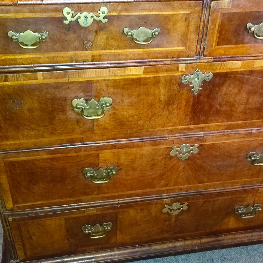 An early eighteenth-century walnut chest of drawers featuring decorative brass handles, crossbanded drawer fronts, and turned bun feet, constructed in two separate upper and lower sections. View II
