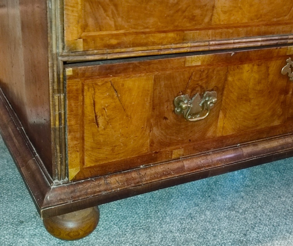 An early eighteenth-century walnut chest of drawers featuring decorative brass handles, crossbanded drawer fronts, and turned bun feet, constructed in two separate upper and lower sections. View III