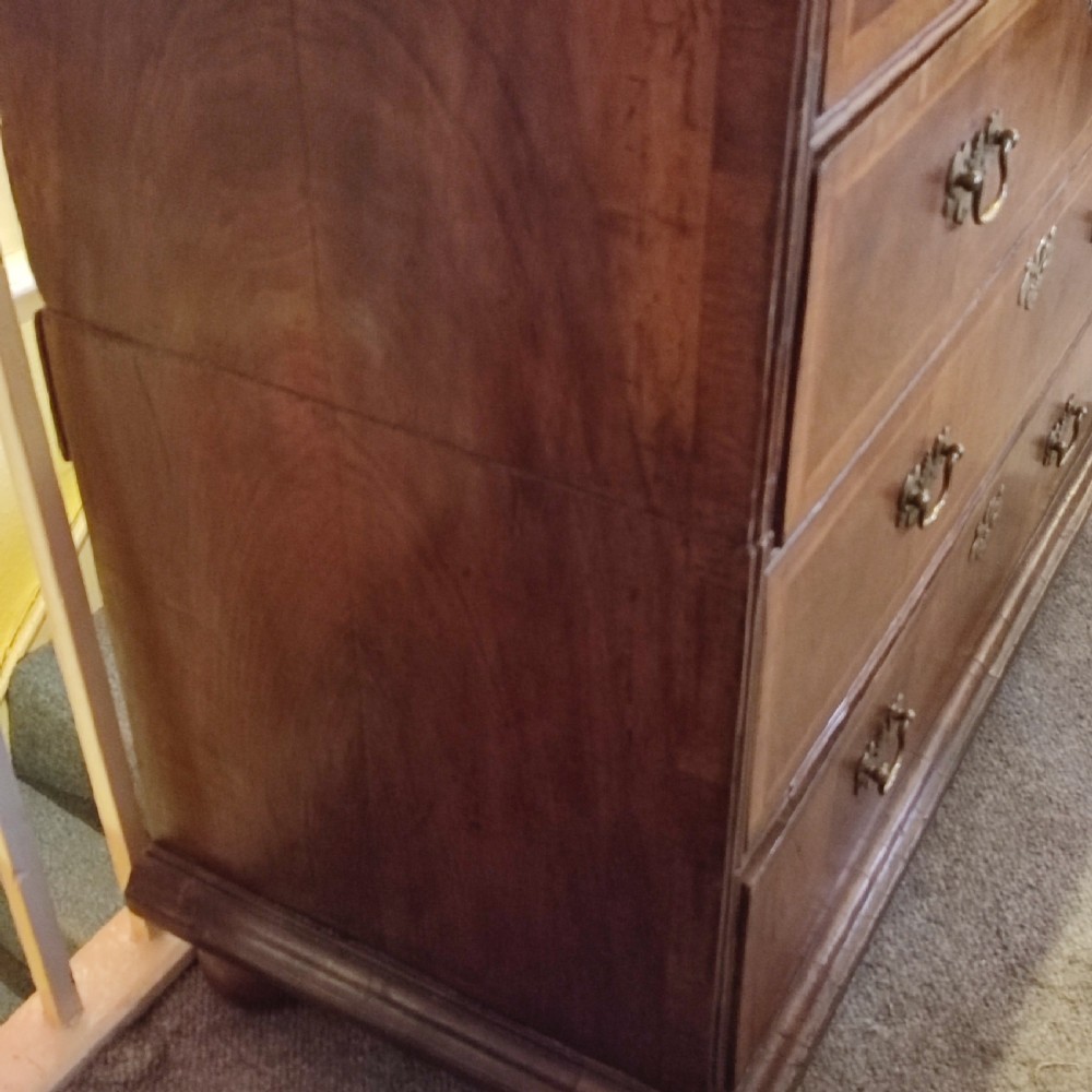 An early eighteenth-century walnut chest of drawers featuring decorative brass handles, crossbanded drawer fronts, and turned bun feet, constructed in two separate upper and lower sections. View V