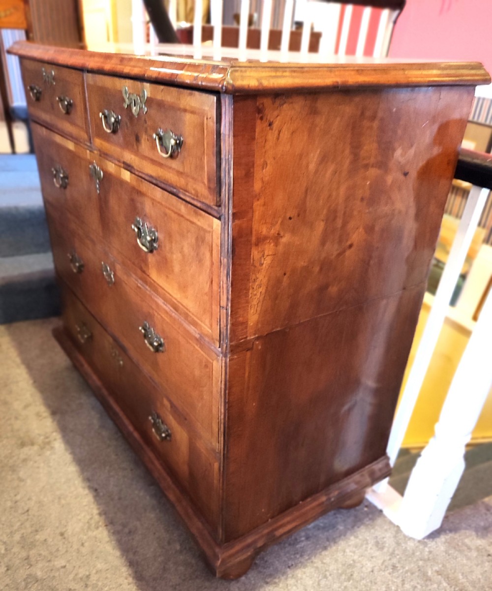 An early eighteenth-century walnut chest of drawers featuring decorative brass handles, crossbanded drawer fronts, and turned bun feet, constructed in two separate upper and lower sections. View VIII