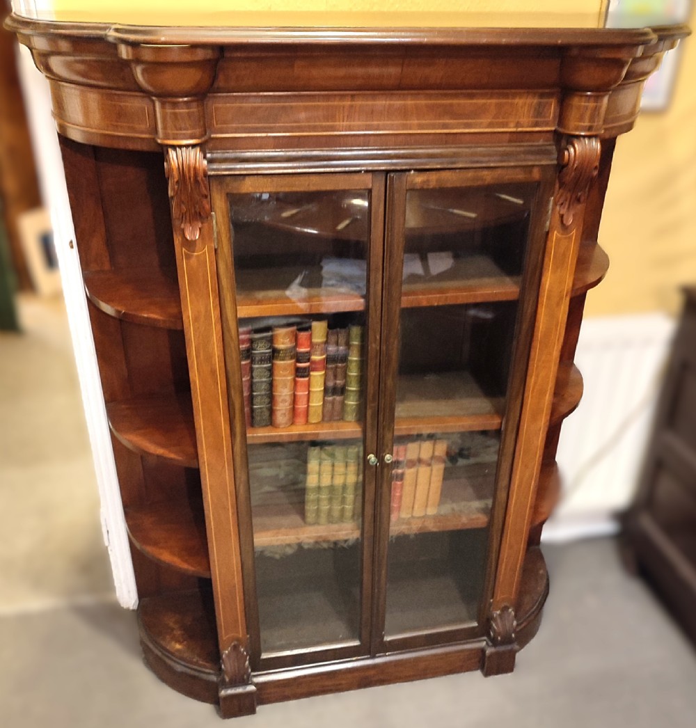An antique Victorian walnut glazed bookcase featuring double glass doors flanked by open curved side shelves and carved corbels.