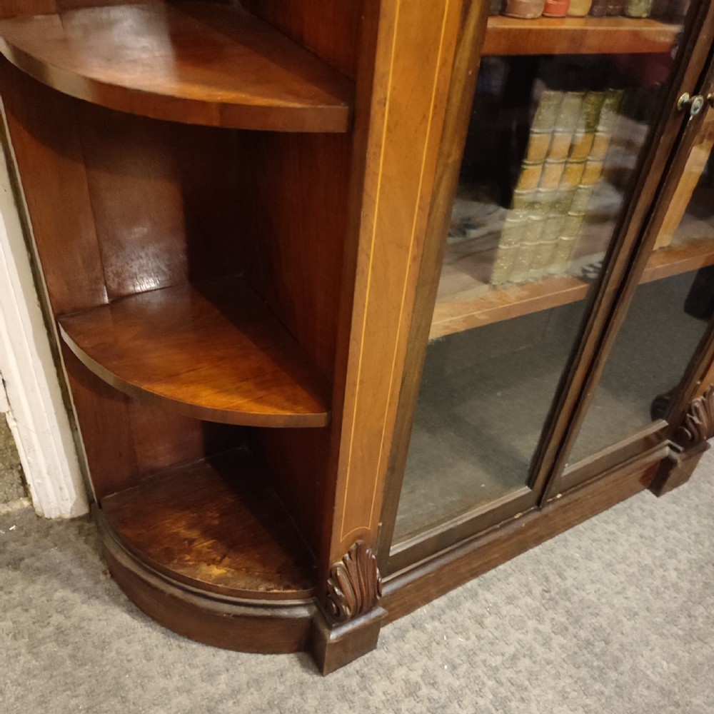 An antique Victorian walnut glazed bookcase featuring double glass doors flanked by open curved side shelves and carved corbels. View III
