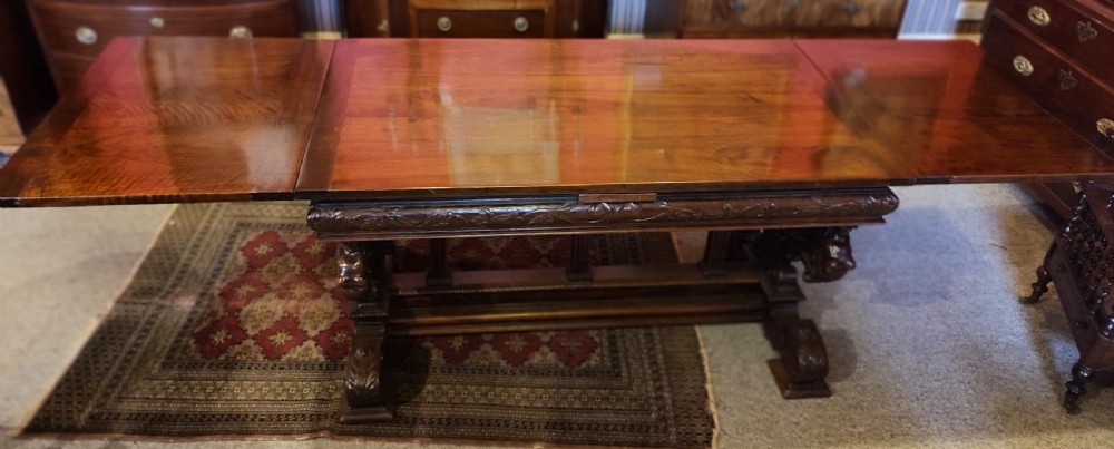 A 19th-century dark walnut extending dining table featuring a polished rectangular top with fully extended side leaves, supported on a heavily carved stretcher base.