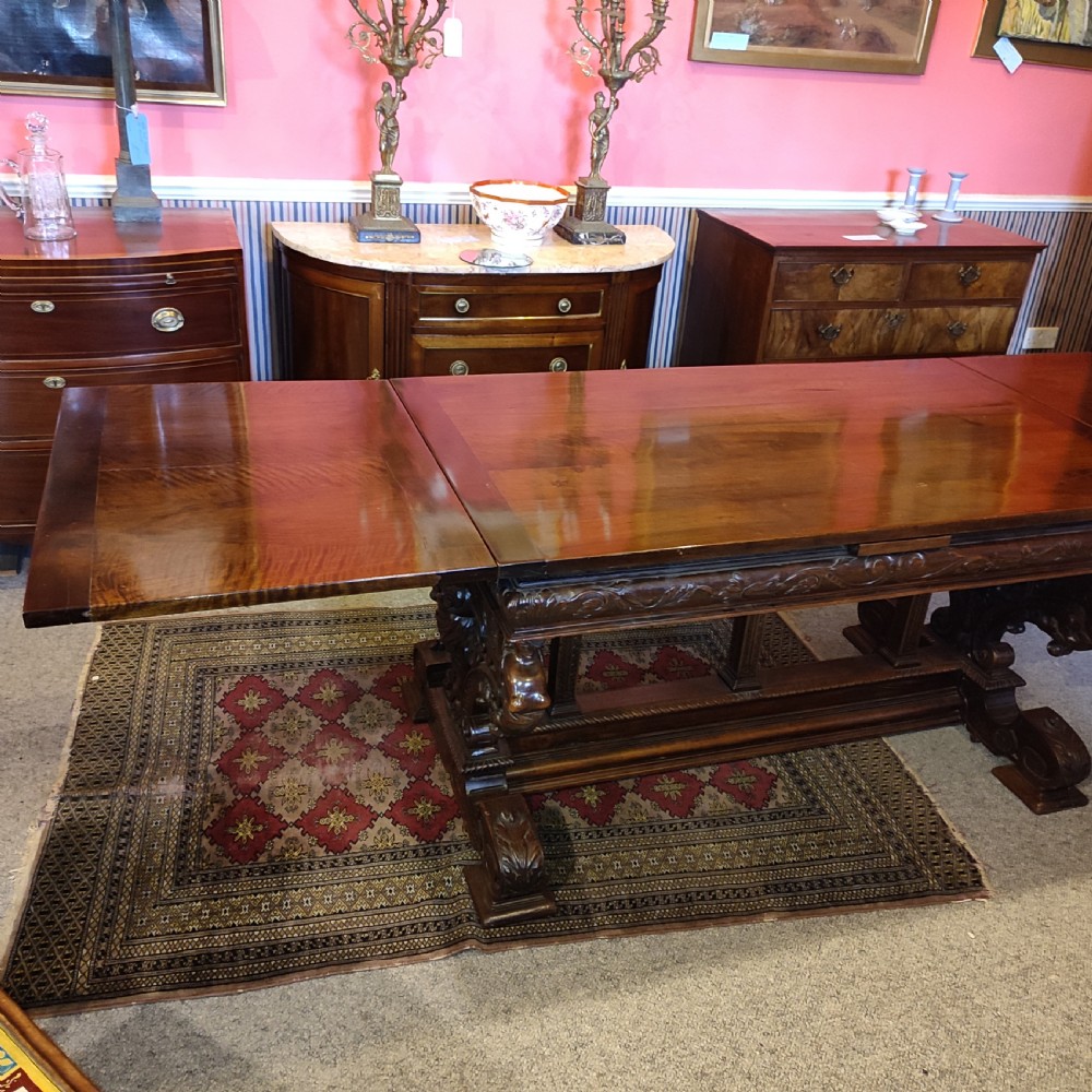 A 19th-century dark walnut extending dining table featuring a polished rectangular top with fully extended side leaves, supported on a heavily carved stretcher base. View VI