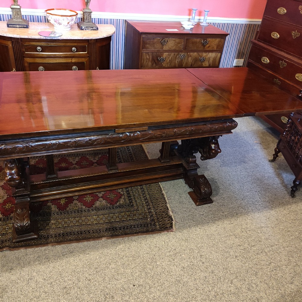 A 19th-century dark walnut extending dining table featuring a polished rectangular top with fully extended side leaves, supported on a heavily carved stretcher base. View VII