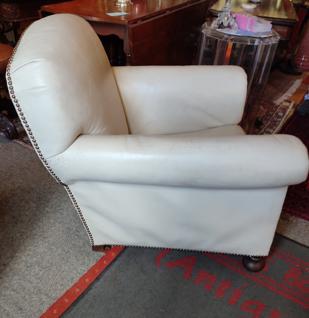 A cream leather Edwardian club chair featuring brass studding along the front edges and resting on short turned wooden feet. View IV