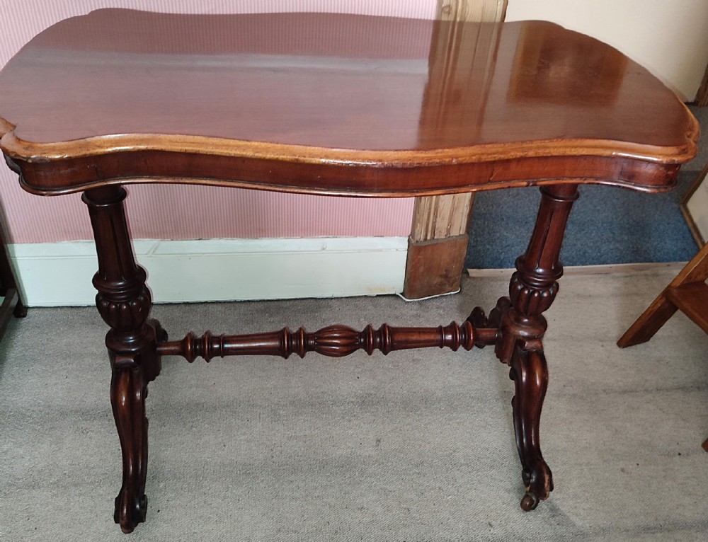A Victorian walnut centre table with a shaped polished top, turned twin-column supports, a carved central stretcher, and cabriole legs with castors.