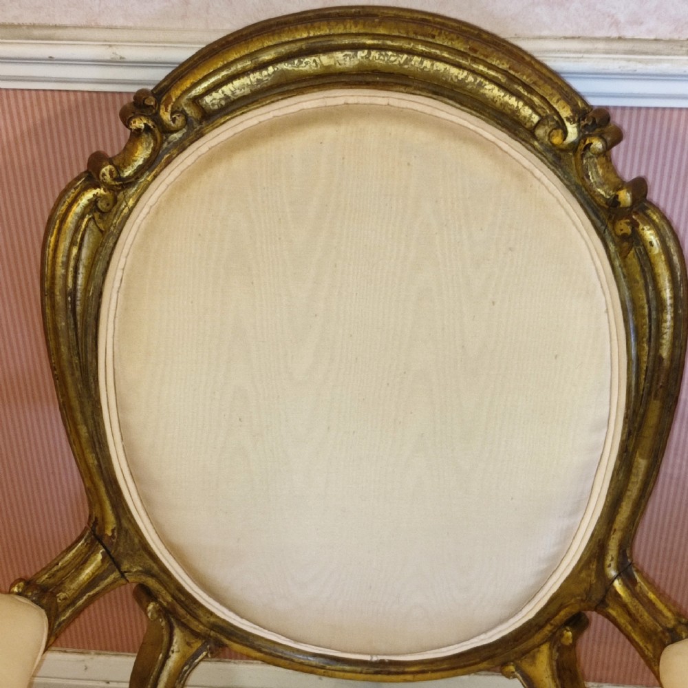 A pair of 19th-century giltwood armchairs featuring carved gold frames, oval backrests, padded arms, cabriole legs, and light cream upholstery. View VI