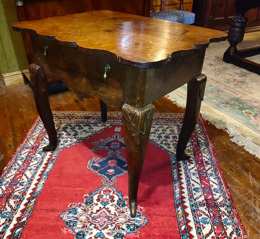An 18th-century oak lowboy featuring a scalloped edge top, a single drawer with brass drop handles, a shaped apron, and carved cabriole legs. View II