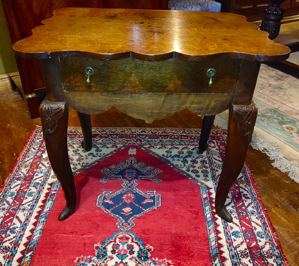 An 18th-century oak lowboy featuring a scalloped edge top, a single drawer with brass drop handles, a shaped apron, and carved cabriole legs. View III