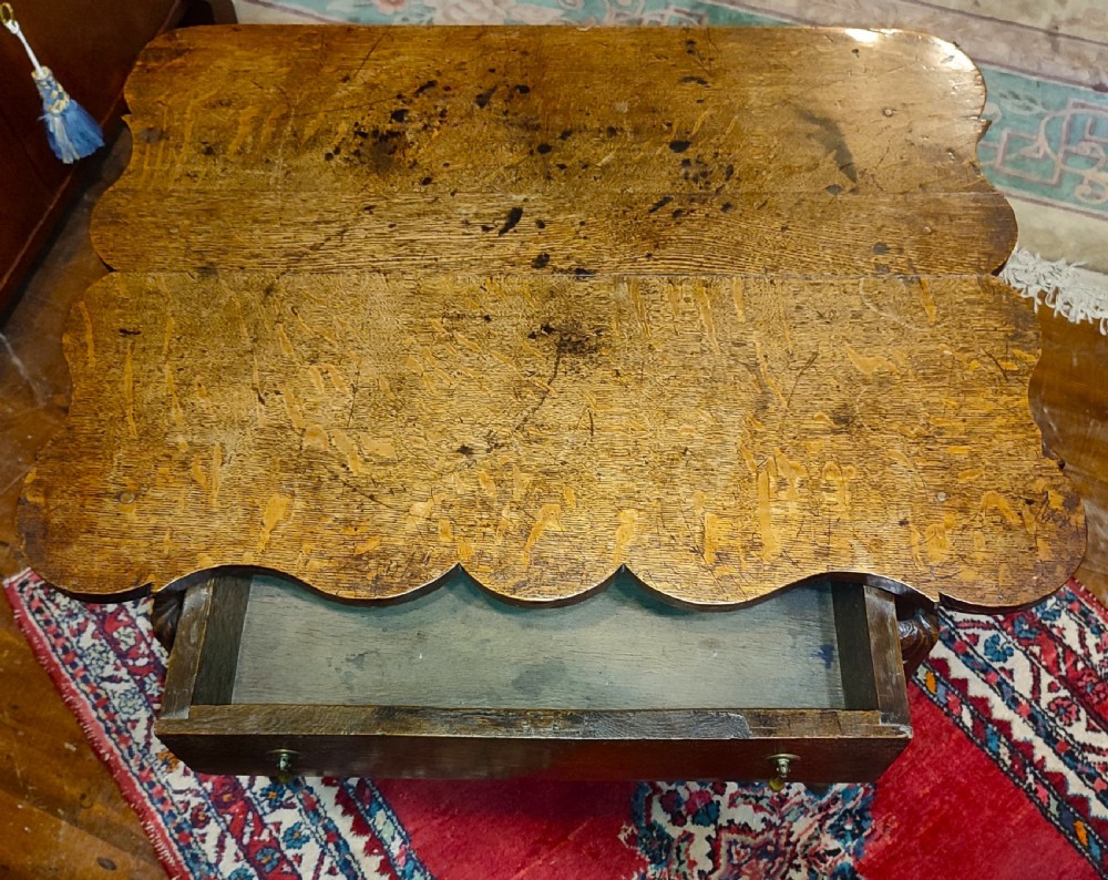 An 18th-century oak lowboy featuring a scalloped edge top, a single drawer with brass drop handles, a shaped apron, and carved cabriole legs. View V