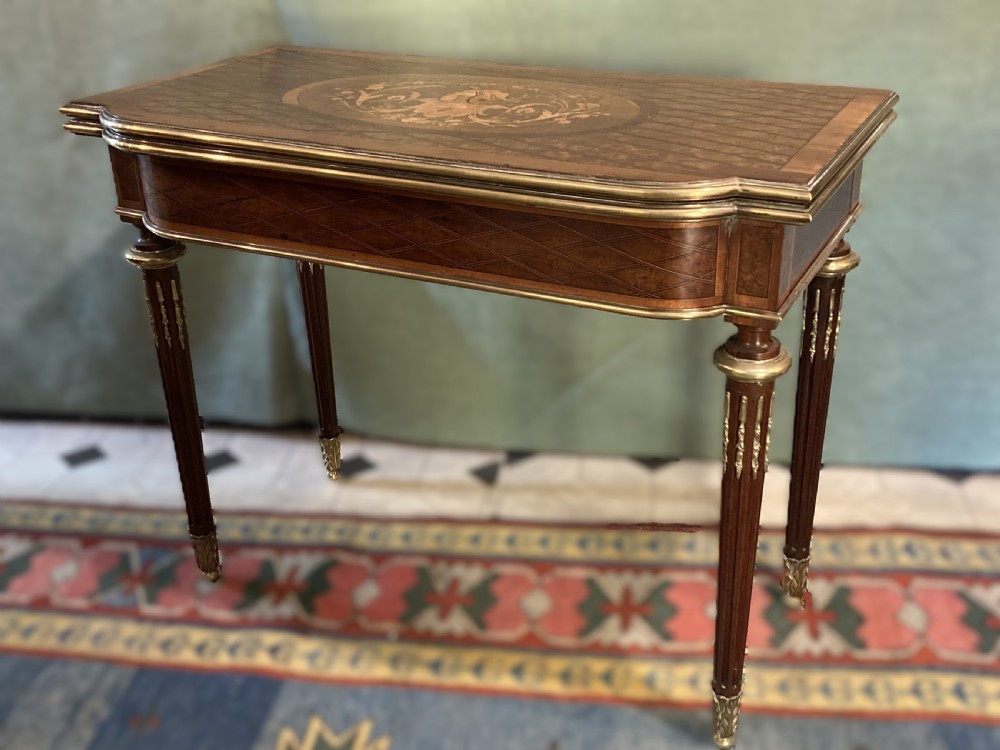 A 19th-century walnut card table featuring a floral marquetry top, brass ormolu trim, fluted tapering legs, and a hinged flip-top.