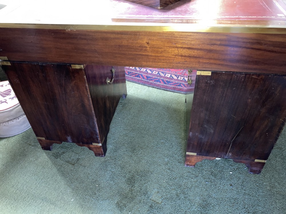 An Edwardian mahogany campaign pedestal desk featuring flush-fitting brass handles, protective brass corner mounts, and a red leather inset writing surface. View III