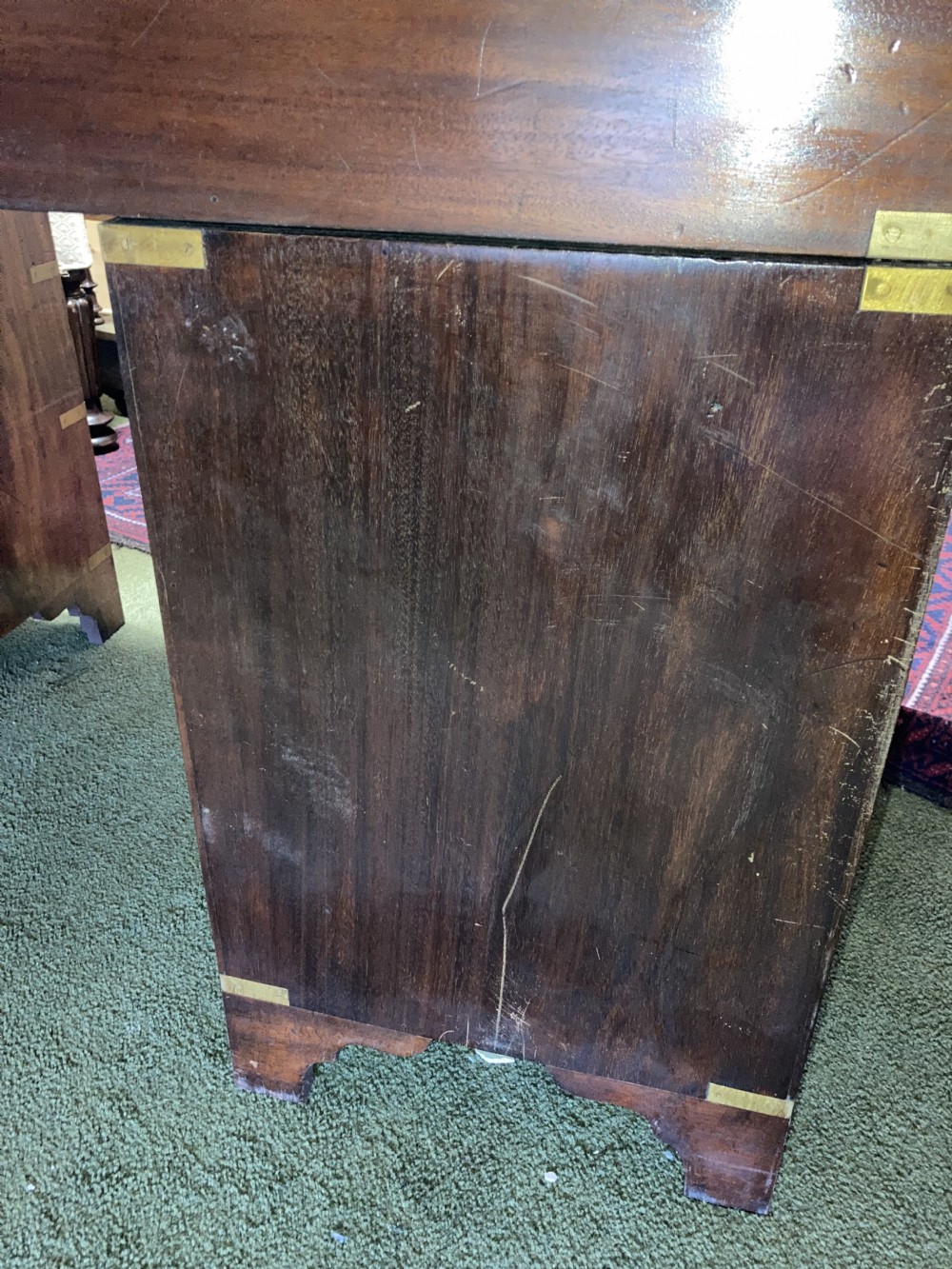 An Edwardian mahogany campaign pedestal desk featuring flush-fitting brass handles, protective brass corner mounts, and a red leather inset writing surface. View IV