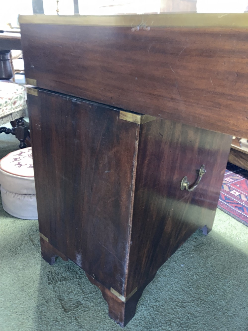 An Edwardian mahogany campaign pedestal desk featuring flush-fitting brass handles, protective brass corner mounts, and a red leather inset writing surface. View V