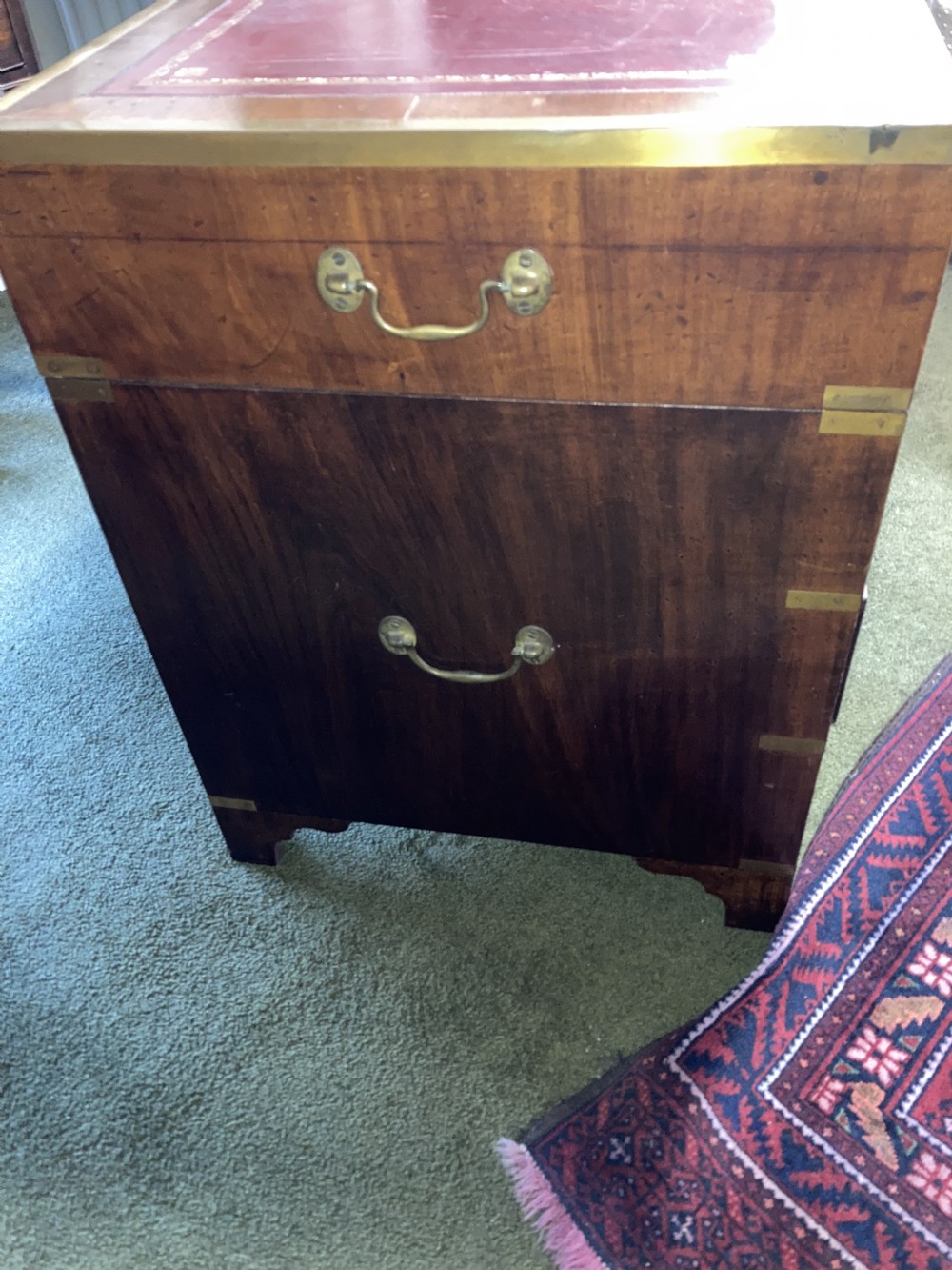 An Edwardian mahogany campaign pedestal desk featuring flush-fitting brass handles, protective brass corner mounts, and a red leather inset writing surface. View VII