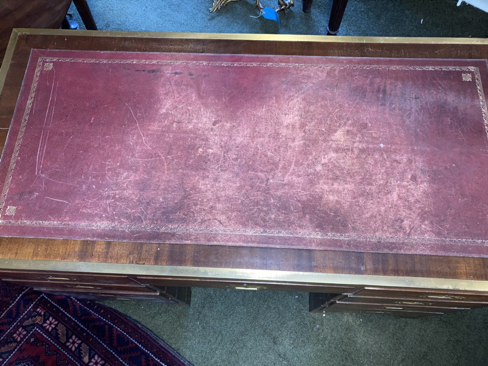 An Edwardian mahogany campaign pedestal desk featuring flush-fitting brass handles, protective brass corner mounts, and a red leather inset writing surface. View VIII
