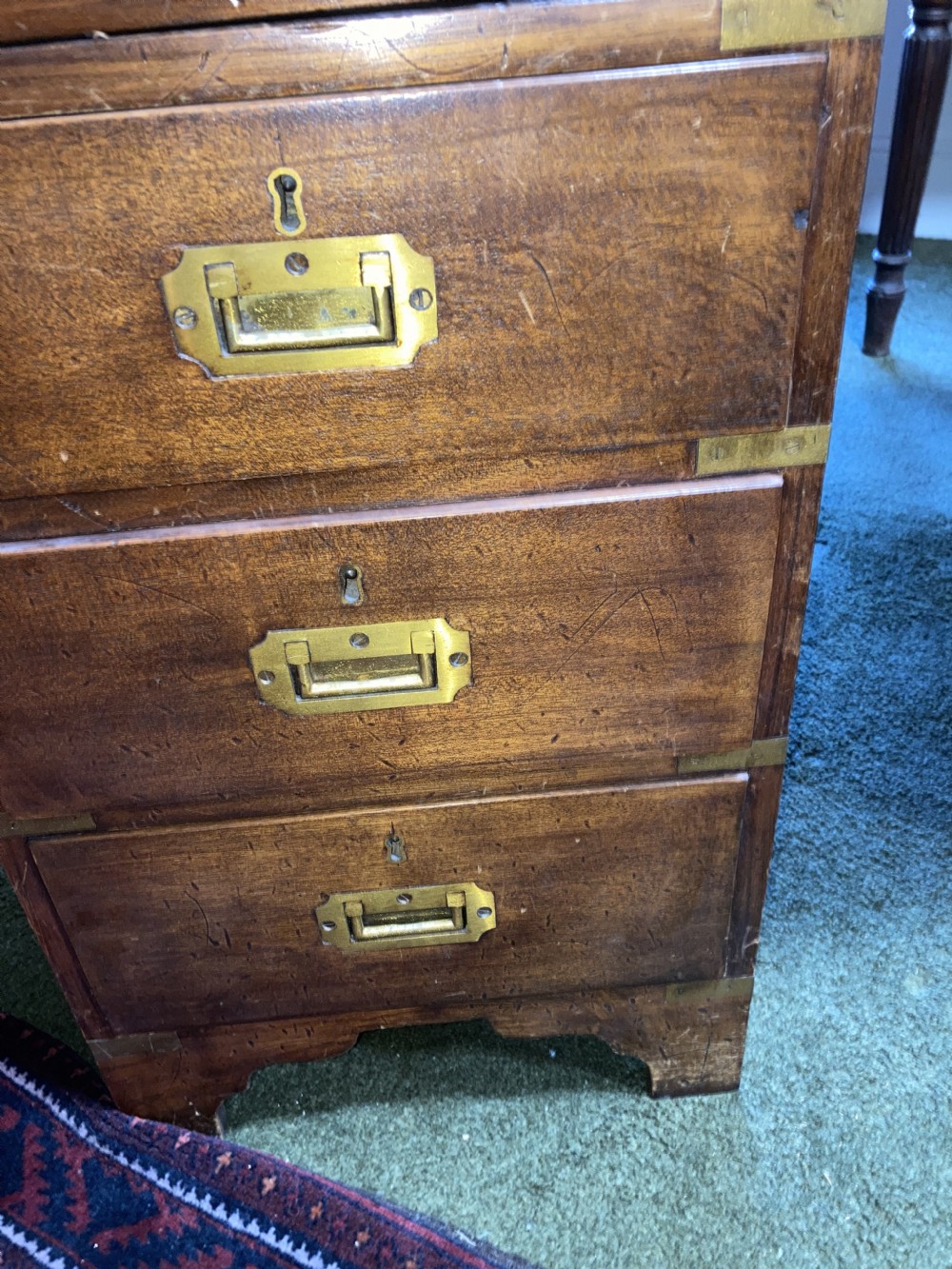 An Edwardian mahogany campaign pedestal desk featuring flush-fitting brass handles, protective brass corner mounts, and a red leather inset writing surface. View IX