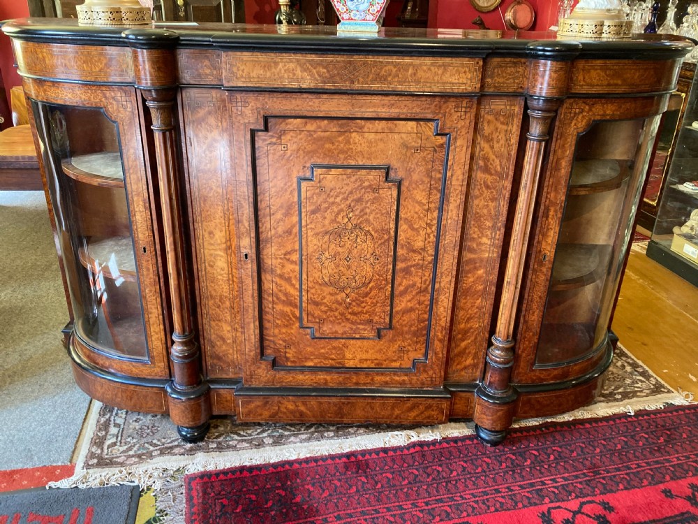 A Victorian amboyna and ebonised credenza featuring a central inlaid door panel, turned columns, and curved glass side doors.