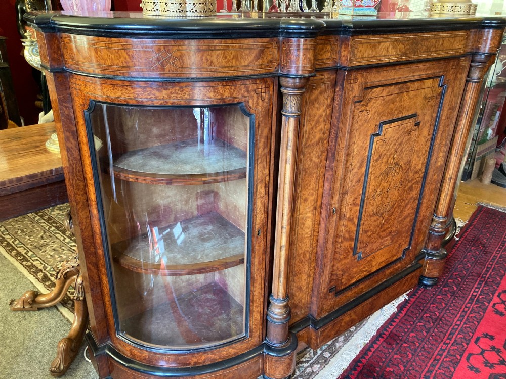 A Victorian amboyna and ebonised credenza featuring a central inlaid door panel, turned columns, and curved glass side doors. View II