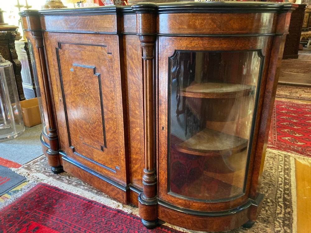 A Victorian amboyna and ebonised credenza featuring a central inlaid door panel, turned columns, and curved glass side doors. View VI