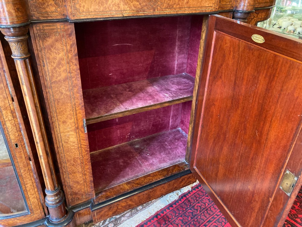 A Victorian amboyna and ebonised credenza featuring a central inlaid door panel, turned columns, and curved glass side doors. View VII