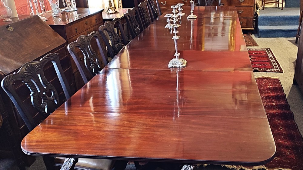 A long, highly polished George III mahogany triple pedestal dining table featuring rounded edge corners and central support columns.