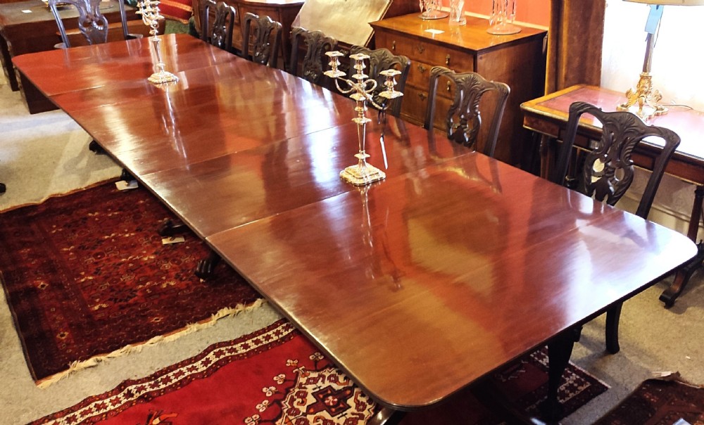 A long, highly polished George III mahogany triple pedestal dining table featuring rounded edge corners and central support columns. View II