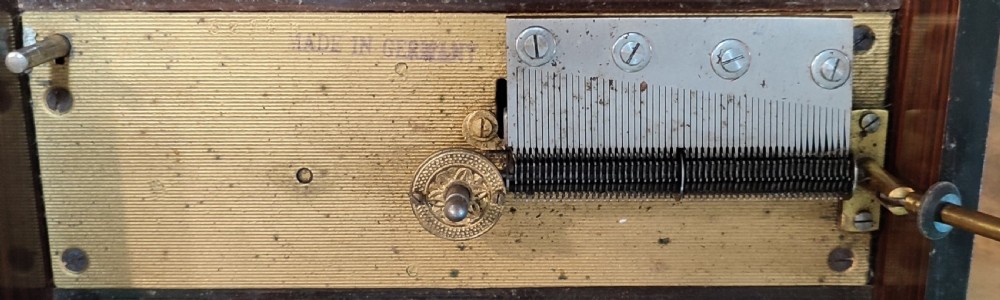 An open 19th-century walnut Polyphon music box featuring a metal disc, central pressure arm, winding crank, and a monochrome print of cherubs on the underside of the lid. View IV