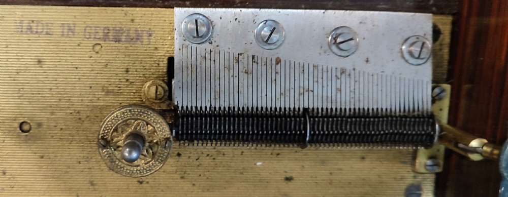 An open 19th-century walnut Polyphon music box featuring a metal disc, central pressure arm, winding crank, and a monochrome print of cherubs on the underside of the lid. View V