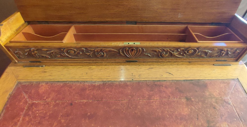 A Victorian 19th-century pollard oak Davenport desk featuring a slanted leather writing surface, carved foliage friezes, and side drawers with brass handles. View V