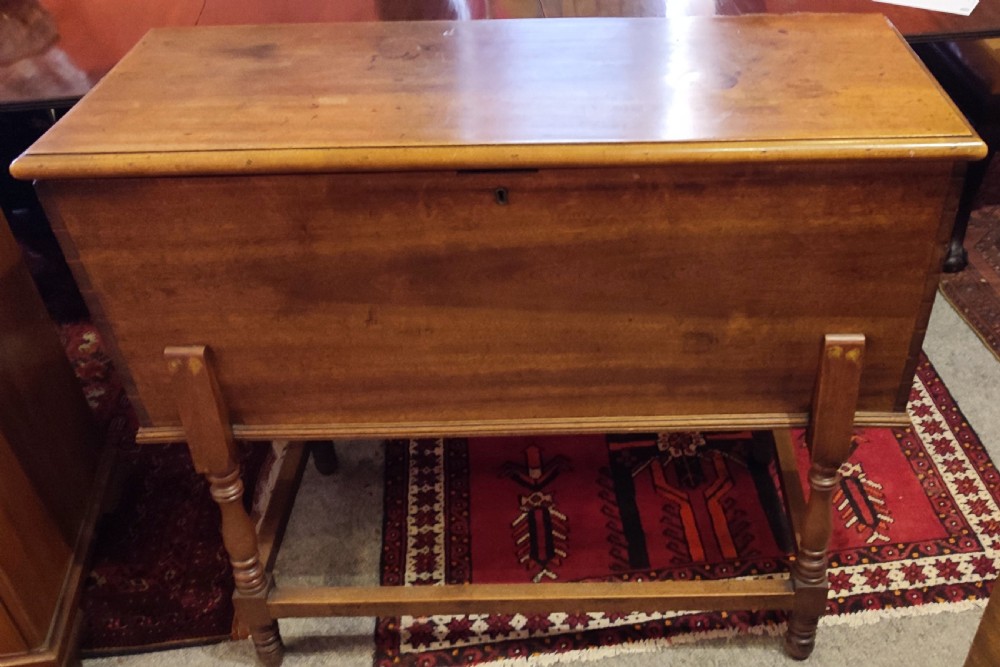 A 19th-century walnut dough bin featuring a rectangular hinged lid, clean panelled sides, an iron keyhole escutcheon, turned lower legs, and horizontal stretchers.